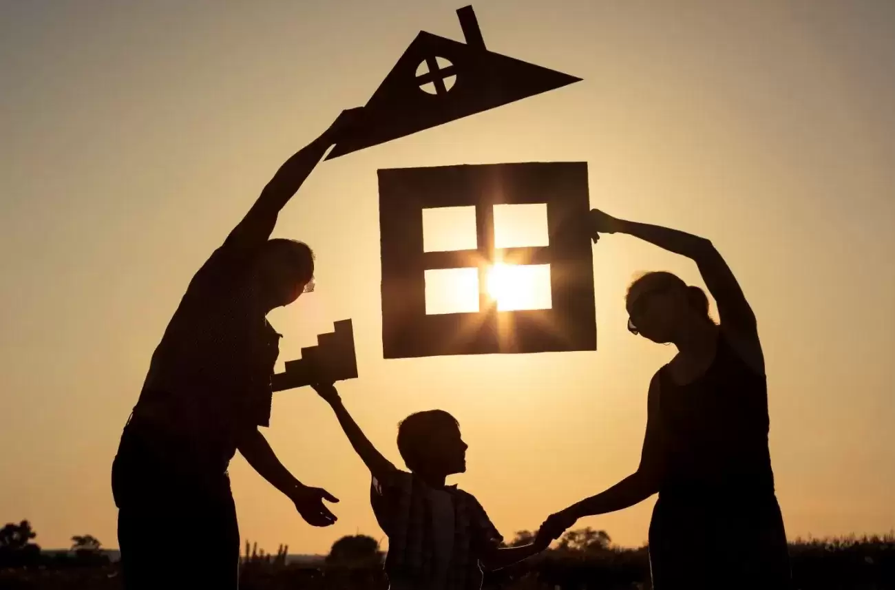 A family holding parts of a house in silhouette to the sun